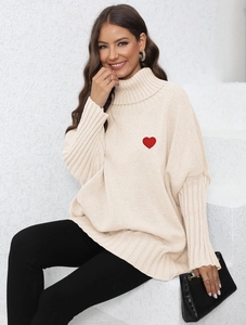 Detail of red heart embroidery on an oversized cream turtleneck knit sweater