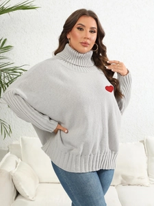 Close-up of light grey turtleneck sweater featuring a red heart patch and ribbed knit cuffs