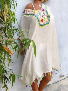 Detail of colorful hand-crocheted neckline and tassel hem on beige boho beach cover-up