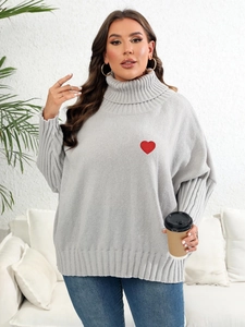 Detail of grey oversized turtleneck sweater with a red heart patch and cable knit texture
