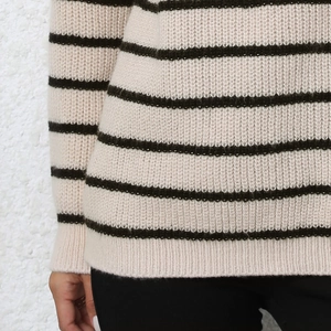 Close-up of the thick striped knit texture and elastic hem on the beige striped sweater