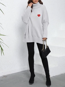 Close-up of light gray oversized knit sweater with red heart embroidery on a street style model