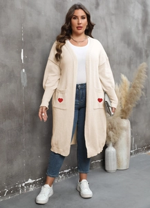 Detail of soft beige knit cardigan featuring large front pockets with red heart embroidery