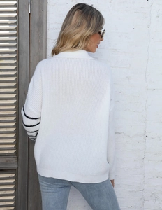 Detail of loose white knit sweater with black stripes on the sleeve and textured fabric