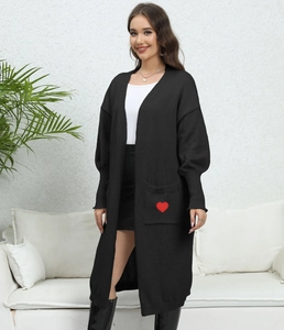Detail of the oversized black knit cardigan featuring red heart patterns on front pockets
