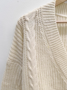 Detail of V-neck knit dress with thick cable stitch pattern on wooden hanger