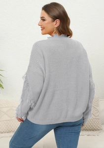 Detail of grey knitted sweater featuring long fringe tassels on sleeves and raw edges