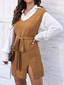 Detail of knit vest dress with side slit and waist belt over a white long sleeve shirt