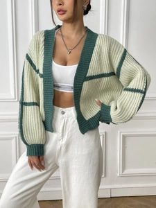 Close-up of green striped knit cardigan with thick texture and high-waist white trousers