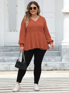 Detail of V-neck rust red ribbed knit tunic with long lantern sleeves and peplum hem