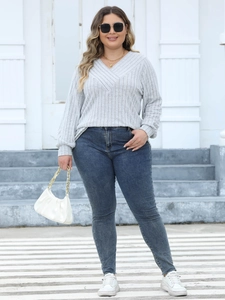 Detail showing women's light grey V-neck ribbed knit sweater and dark blue skinny jeans