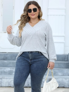 Outdoor shot of a woman in a light grey ribbed V-neck sweater and blue skinny jeans