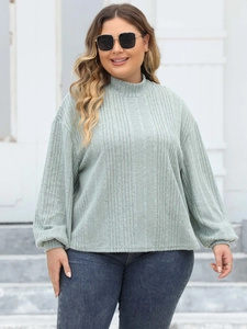 Detail of light green ribbed knit texture and puff sleeve cuffs on a mock neck top