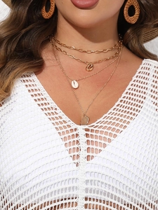 Close-up of layered gold shell necklaces and textured disc charm on a crochet cover-up