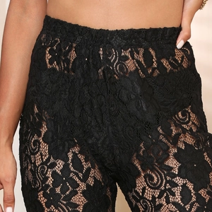 Close-up of the delicate floral lace pattern and elastic high waist of black see-through pants
