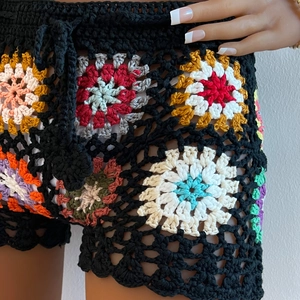 Detail of colorful hand-crocheted granny square patterns on black beach shorts
