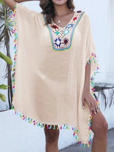 Détail de l'encolure au crochet multicolore et des pompons sur cette robe de plage beige