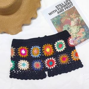 Detail of colorful handmade crochet granny square stitching on black beach shorts