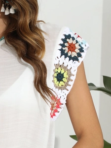 Détail de patchwork floral au crochet coloré sur une robe de plage blanche à pompons