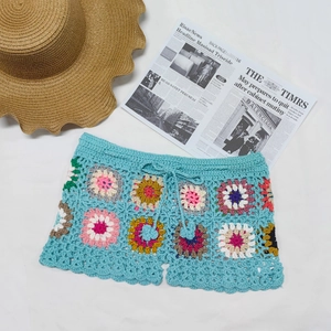 Detail of colorful hand-crocheted beach shorts with bright blue knit and 3D floral patches
