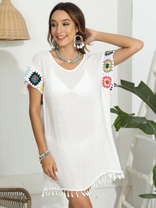 Détails rapprochés des motifs floraux au crochet et des franges sur ce cache-maillot blanc