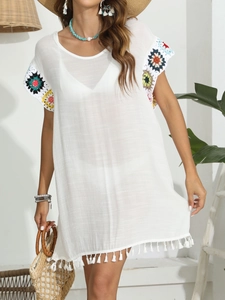 Détail d'une robe de plage bohème blanche avec manches en crochet coloré et bordure à franges