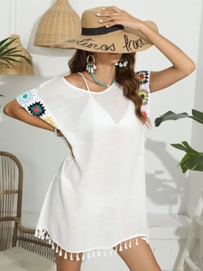 Détail d'une robe de plage blanche avec poignets en crochet coloré et bordure à franges