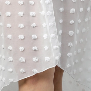 Detailed close-up of white semi-transparent chiffon fabric with textured 3D pom-pom dots