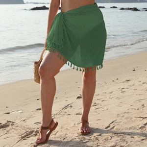 Detail of dark green beach sarong featuring fringe trim and side tie closure on a sunny beach
