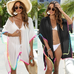 Detail of loose beach cover-up featuring white lace crochet and colorful tassel pom-poms