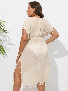 Detail of beige beach cover-up with tassel trim and side slit on a model