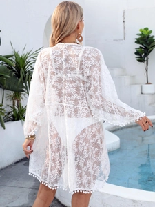 Detailed view of floral lace texture and pompom trim on white sheer beach cover-up