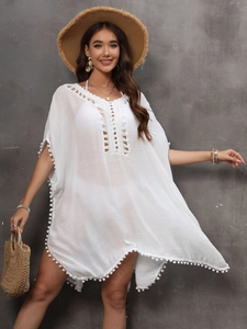 Detail of white crochet beach cover-up featuring pom-pom trim and lace-up neckline