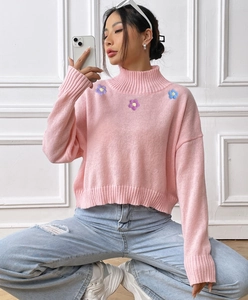 Detail of pink turtleneck knit sweater featuring delicate floral embroidery and ribbed cuffs