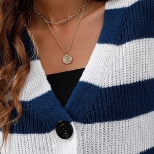 Dettaglio collana a strati dorata con ciondolo a moneta su un cardigan a righe