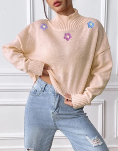 Detail of pink knit sweater featuring mock neck and delicate floral chest embroidery