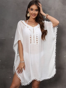 Detail of white beach cover-up featuring deep V lace neckline and pom-pom trim accents