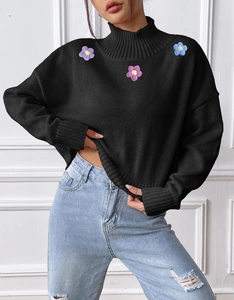 Detailed shot of three colorful 3D crochet flowers on a black high-neck knitted sweater