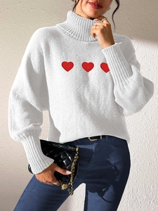 Close-up of white turtleneck sweater with red heart embroidery and ribbed cuffs