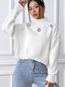 Detail of floral embroidery on a white turtleneck knit sweater with ribbed cuffs