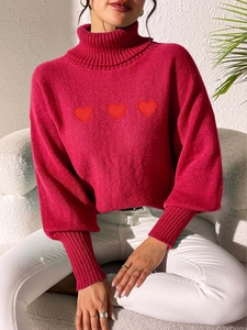 Detail of a bright fuchsia knit sweater featuring three red heart embroidery patches