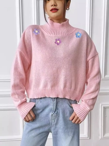 Pink high-neck knit sweater with floral embroidery paired with light blue jeans
