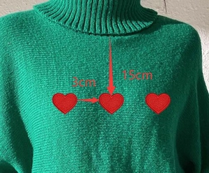 Detail view of green turtleneck sweater showing three red heart patches with 3cm spacing