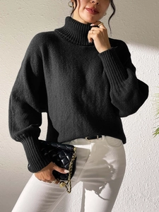 Close-up of black high-neck knit sweater showing ribbed cuffs and drop shoulder texture