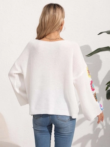 Detail of white knit sweater with colorful crochet floral patches on the sleeves