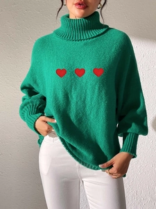 Detail of green turtleneck sweater showing three red embroidered hearts and knit texture