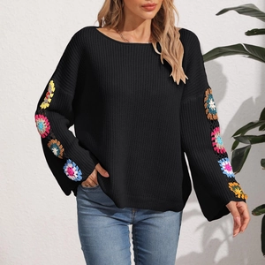 Detailed close-up of colorful crochet floral patchwork on black knit sweater sleeves