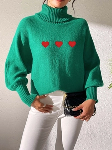 Close-up of green turtleneck sweater with red heart embroidery and ribbed cuffs