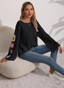 Detail of colorful crochet floral patterns on black bohemian knit sweater sleeves