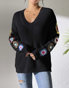 Detail of V-neck sweater sleeve with colorful crochet floral patchwork and knit texture